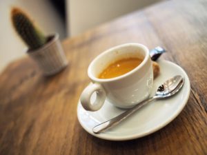 A double espresso sits in a small white cup on a dark wooden table with a small cactus plant in the background at Cassiopee Cafe in Paris