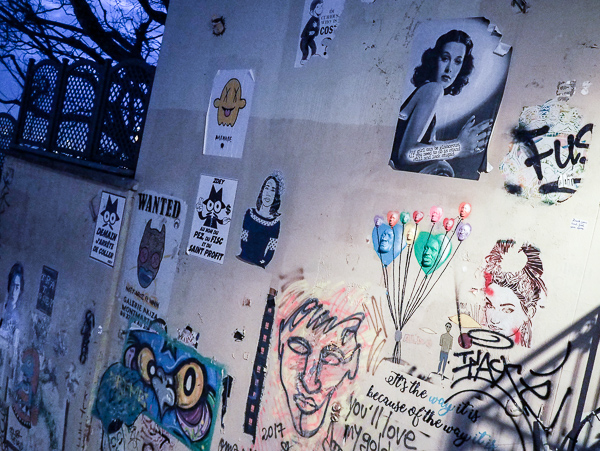 A large exterior wall of Paris Street Art in Montmartre neighborhood. Wall has over a dozen random stencils, drawings, and wheat paper murals on it.