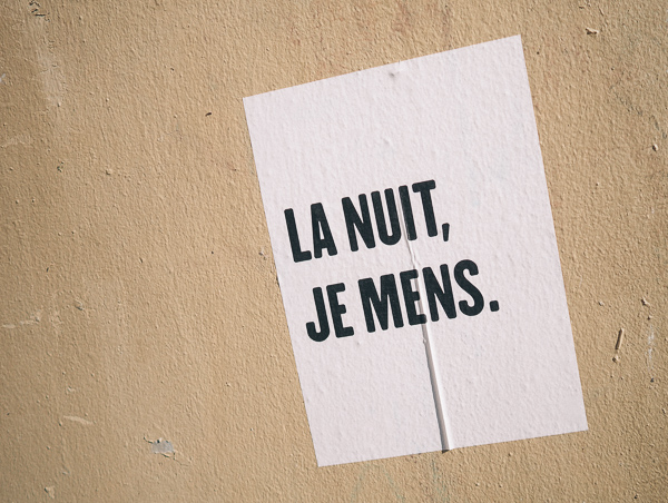 Paris street art of simple white background with black block letters reading "La Nuit, Je Mens." or "The Night, I Lie" - lyrics from an Alain Bashung Song