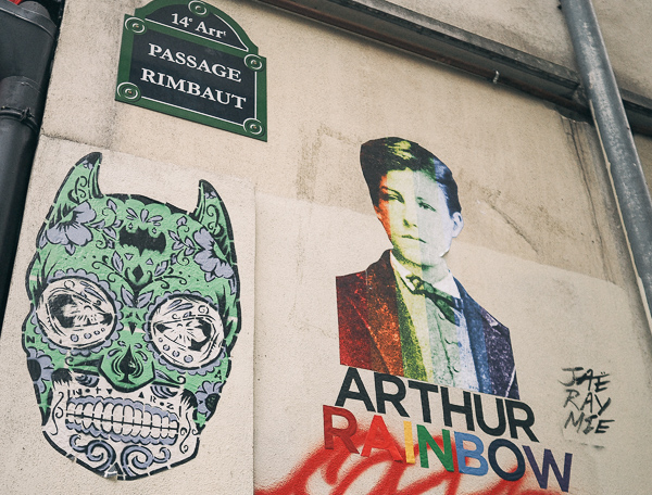 Two pieces of street art at Passage Rimbaut in Paris - one is a picture of Arthur Rimbaud that says Arthur Rainbow below it. The letters that make up Rainbow are each in a different color. The other image is a mix of Batman's Catwoman with Mexican Dias de los Muertos makeup called Wanted by street artist "Wanted" Catwoman by El Murcielago.