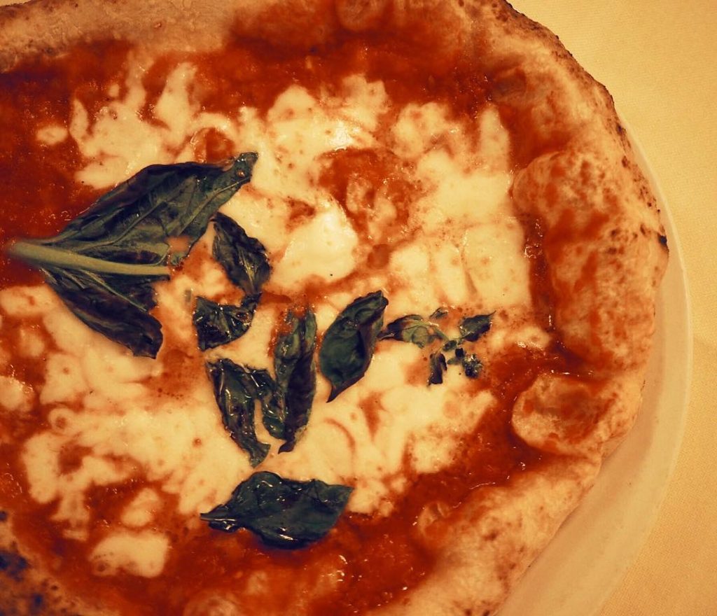 A photo of a fresh out of the oven margherita pizza with tomato sauce, basil, and mozzarella as made by the restaurant that first created the recipe for Queen Margherita in Naples, Italy - Pizzeria Brandi