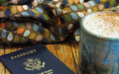 A picture of my first United States Passport with an almond milk latte in a ceramic mug beside it and a scarf with softly colored stylistic leaves on it in the background