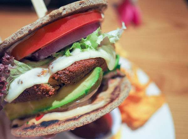 Picture shows Avocado Restaurant's Signature Veggie Burger, loaded with avocado, slices of tomato, lettuce, and quinoa black bean patty topped with cheese on a sprouted flatbread "bun") and a side of sweet potato chips