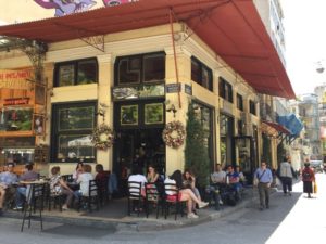 exterior photo of Nancy's Sweet Home pastry and cake shop in Athens Greece. Picture shows people sitting at cafe tables out front and on the side of the corner bakery. Photo taken by Janao of Norway.